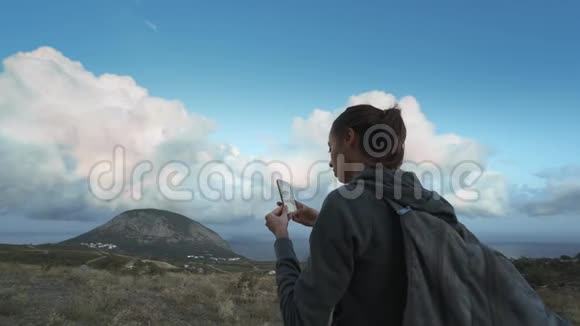 女徒步旅行者看着美丽的多云的日落天空用手机拍照视频的预览图