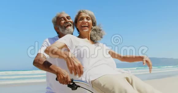 活跃的非洲裔美国老年妇女坐在沙滩上的男子自行车把手的正面景色视频的预览图