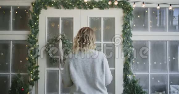 穿暖和毛衣的女人用圣诞花环装饰大门装饰圣诞屋舒适的新房子视频的预览图