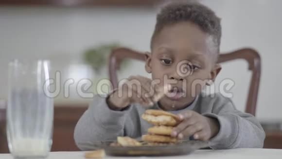 可爱的非洲裔美国儿童的肖像在牛奶制作后嘴唇脏饼干金字塔坐在桌子旁视频的预览图