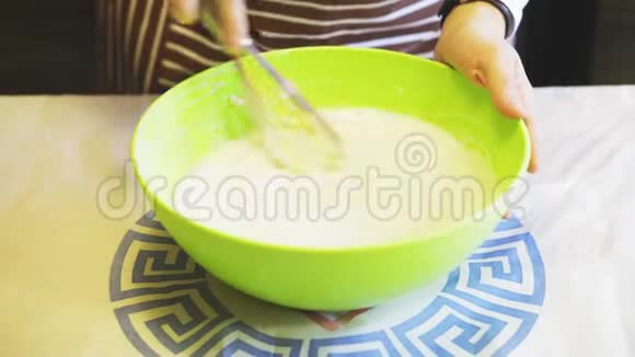 在家庭厨房的绿色碗中女性手的特写将面糊和厨房搅拌器混合在一起烹饪煎饼视频的预览图