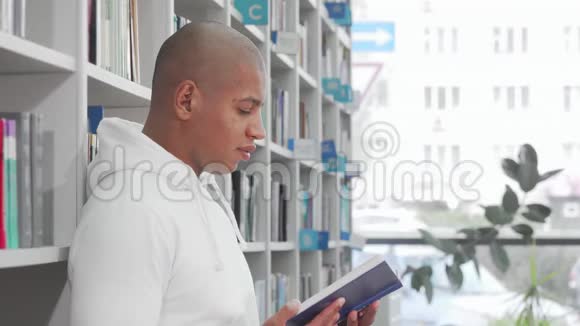 英俊的非洲男人在图书馆看书时对着镜头微笑视频的预览图