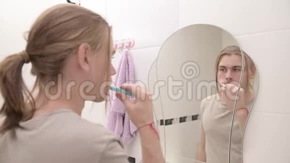 年轻迷人的千禧一代长发男子保持早晨的口腔卫生在浴室里用镜子刷牙视频的预览图
