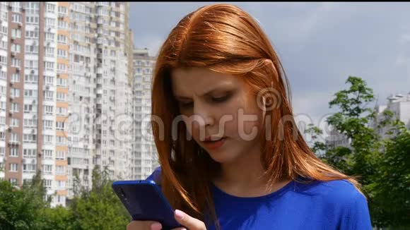 年轻漂亮的红发女孩在城市里用手机在城市里寻找信息视频的预览图