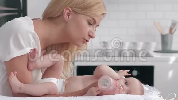 可爱的妈妈在厨房的换桌上给刚出生的女孩喝水然后亲吻她的双手视频的预览图