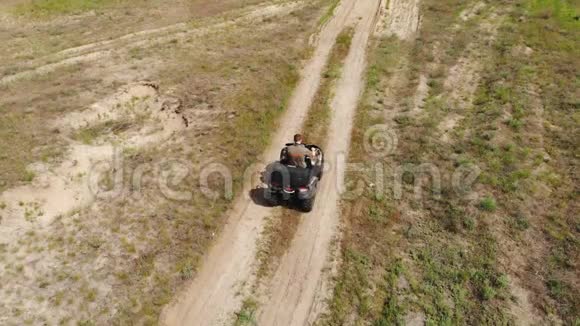 从上到下的空中俯瞰年轻的成年人骑着一辆ATV四轮自行车在乡间崎岖的地形道路上草地干燥视频的预览图