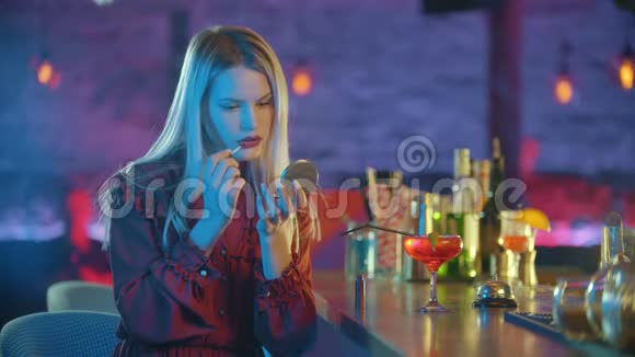 漂亮的金发女郎坐在酒保的旁边嘴唇上涂着红色的口红视频的预览图