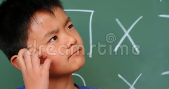 4k教室体贴的亚洲男生在黑板上挠头的正面图视频的预览图