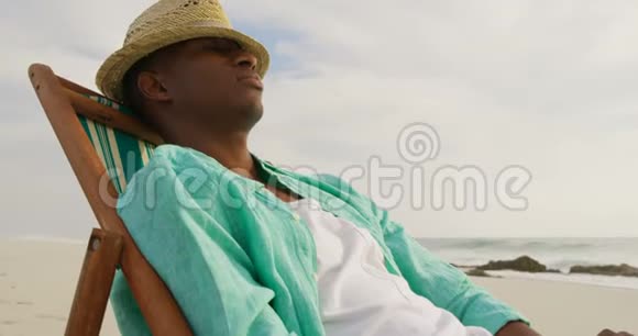 美国黑人男子睡在海滩上的阳光休息室的侧面景色视频的预览图