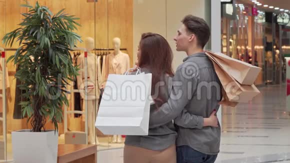 后景拍摄一对夫妇拿着购物袋在商场寻找一家商店视频的预览图