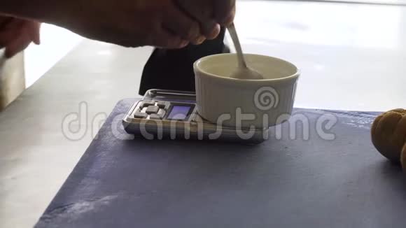 厨师在厨房的天平上用一个陶瓷形状的汤匙撒上一些东西然后用手做特写视频的预览图