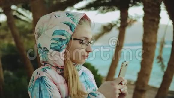 戴眼镜的年轻金发女子通过电话拍照强风背景是大海和手掌动作缓慢4k视频的预览图