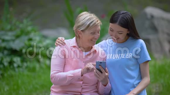 成熟的女性和年轻的志愿者一起看智能手机照片协助视频的预览图