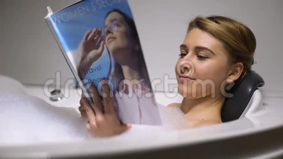 美丽的女人在浴缸里用泡沫泡读杂志晚上放松视频的预览图