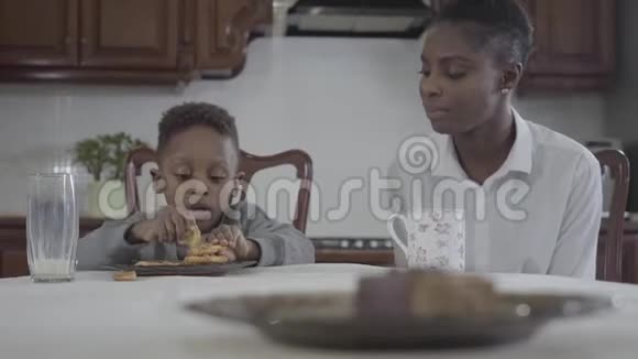 漂亮的非裔美国女人和她的小儿子坐在桌子旁在盘子里玩饼干关系视频的预览图