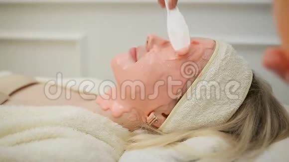 一个近景的女人她的脸与粉红色面具美容师清洁面膜剥皮美和身体护肤视频的预览图