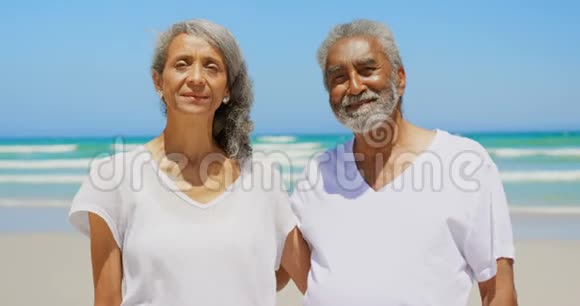 正面观看活跃的非裔美国人夫妇手臂环抱站在海滩4k视频的预览图