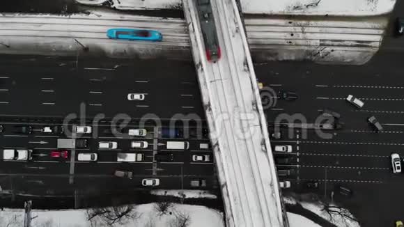 在一条冬季道路上有大量的汽车和公共汽车蓝色有轨电车和灰色火车的空中俯视交通堵塞视频的预览图