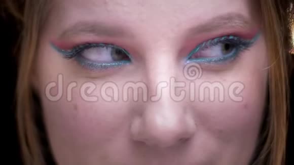 一张金发模特的特写照片她用五颜六色的化妆品在模糊的灯光背景下来回移动眼睛视频的预览图