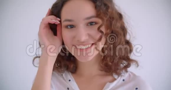 特写镜头年轻美丽的白种人卷曲的女性笑着开心地修着头发看着摄像机视频的预览图