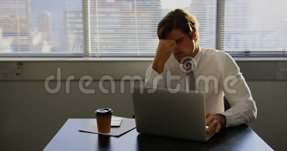 疲惫的白人男性高管在现代办公室的办公桌上用笔记本电脑工作视频的预览图