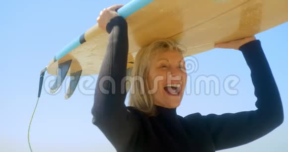 积极向上的高加索族女性冲浪者在海滩头上拿着冲浪板的正面景色视频的预览图