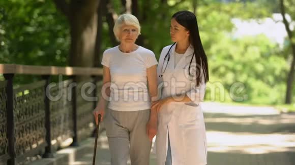 医生和精神错乱的老年女性病人在医院公园散步健康视频的预览图