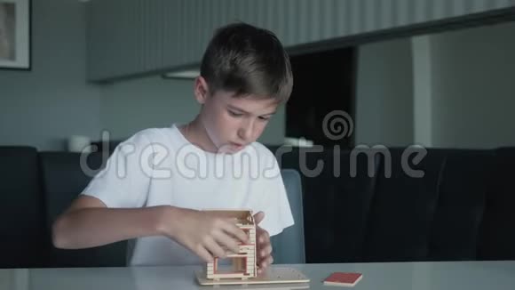 这个男孩收集了一个坐在桌子旁的房子的木制模型视频的预览图