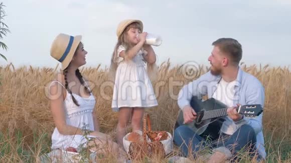 一家人在野外度假年轻的父亲弹吉他和妻子一起嘲笑女儿喝酒舔牛奶胡须视频的预览图