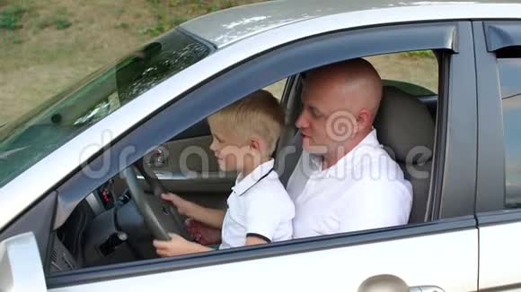 一个年轻的父亲教他的小儿子开车他们坐在方向盘上视频的预览图