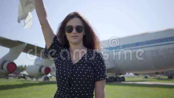 可爱的黑发女孩白色披肩和眼镜在大飞机前面看着相机夏天快乐视频的预览图