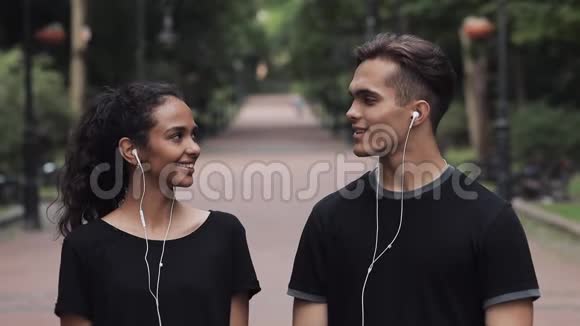 戴着耳机的年轻白种人男子和穆斯林妇女站在公园里扭着头看电影视频的预览图