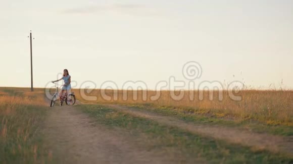 一个小女孩骑自行车在乡间小路上日落时一个女孩骑着一辆小自行车穿过田野视频的预览图