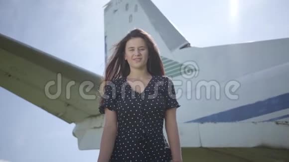 快乐的年轻微笑的黑发女孩看着大白色飞机前面的相机夏天旅行的乐趣视频的预览图