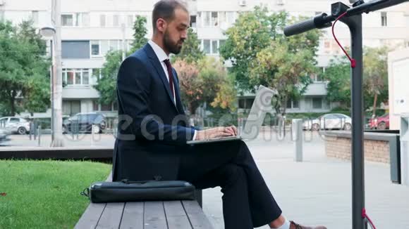 一个穿西装的男人在他所在城市的办公室室外的笔记本电脑上打字视频的预览图