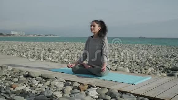 放松运动的女孩坐在靠近大海的木路上沉思视频的预览图