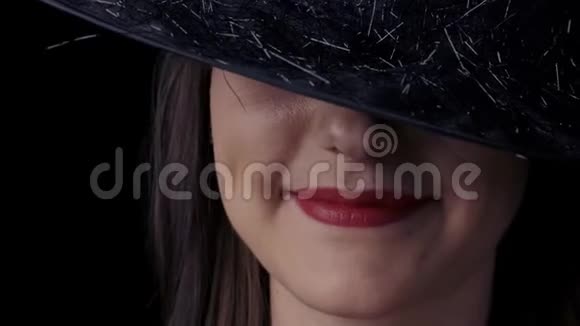 一个戴着黑巫婆帽的迷人神秘女人的半边脸的特写鲜红的嘴唇微笑着视频的预览图