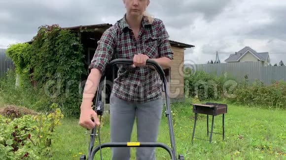 金发女人试图启动割草机的引擎在花园里夏天工作割草视频的预览图
