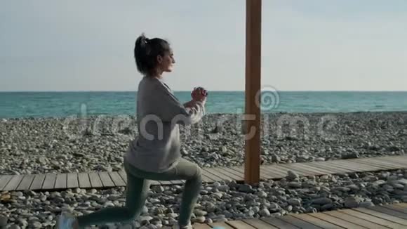 年轻的运动女子正在户外训练靠近空海海岸蹲着视频的预览图