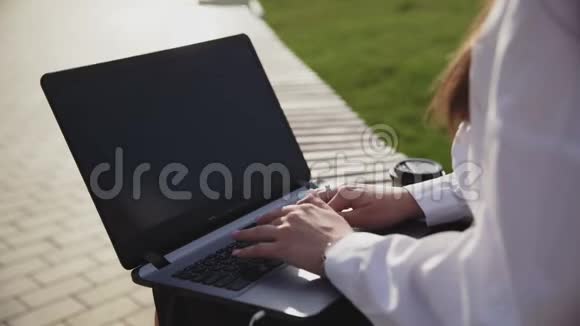 年轻的商务女性坐在户外的长凳上带着笔记本电脑和工作视频的预览图