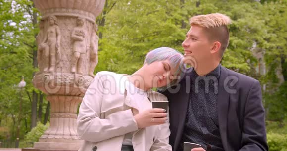 一对年轻漂亮的时髦情侣在户外公园里坐着喝着咖啡享受快乐的特写镜头视频的预览图