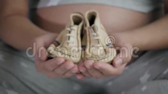 怀孕妇女展示她的双手漂亮的小鞋子为婴儿贴身服务视频的预览图