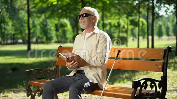 快乐的盲人养老金领取者在盲文书中阅读有趣的故事享受公园的休息视频的预览图