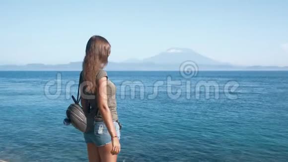 背着背包的女旅行者张开双臂欣赏大海群山视频的预览图