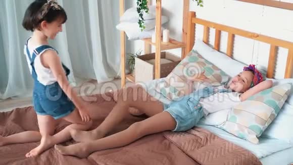 两个快乐的小女孩在床上玩耍互相挠痒笑慢动作视频的预览图