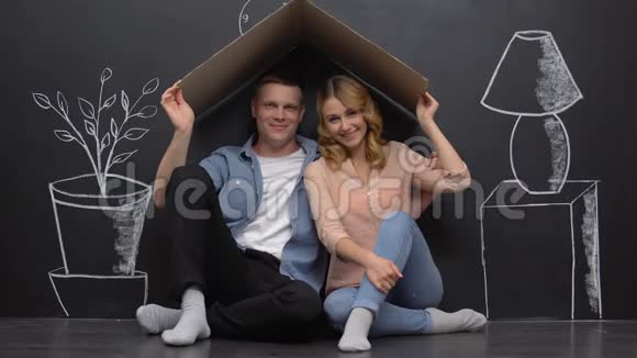 一对微笑的夫妇坐在卡通屋顶下室内设计画在墙上视频的预览图