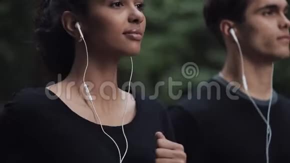 帅气的年轻情侣在耳机里看着轻松的跑步在公园侧景近距离关注女孩视频的预览图