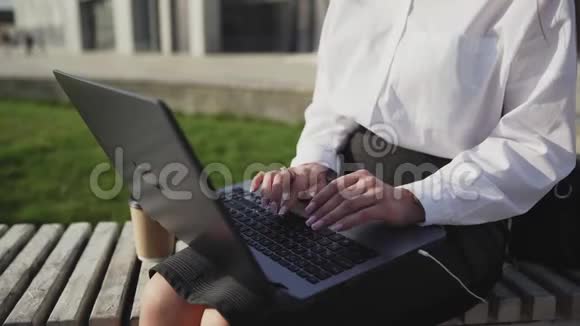 年轻的商务女性坐在户外的长凳上带着笔记本电脑和工作视频的预览图