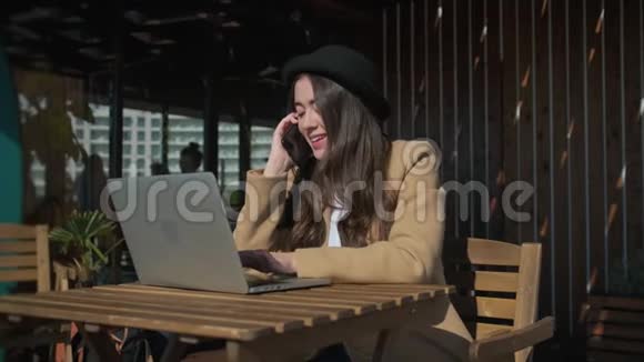 年轻的自由职业者妇女在咖啡馆里用手提电脑和电话交谈视频的预览图