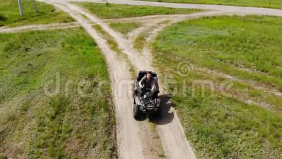 从上到下的空中俯瞰年轻的成年人骑着一辆ATV四轮自行车在乡间崎岖的地形道路上草地干燥视频的预览图